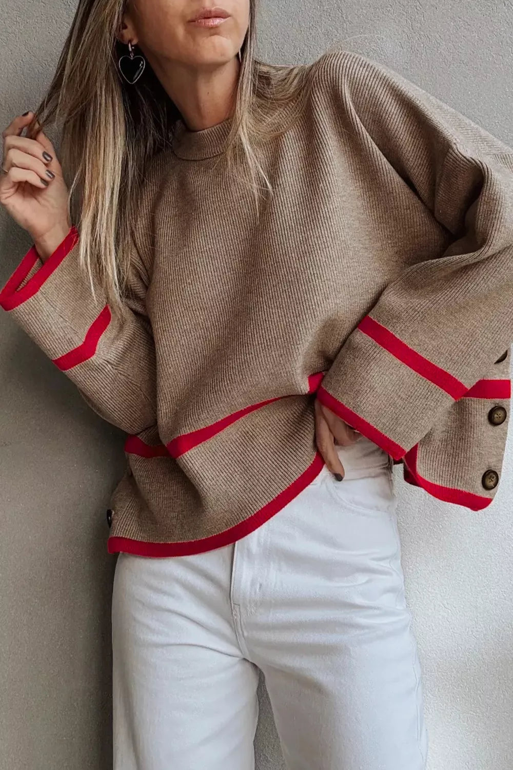 Person wearing a brown sweater with red accents and white pants against a neutral background