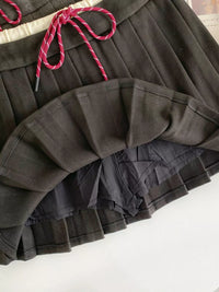 Black pleated skirt with pink drawstring on a white surface