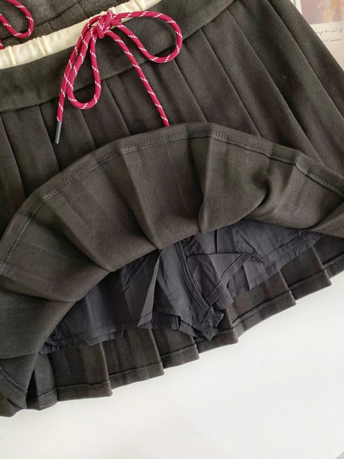 Black pleated skirt with pink drawstring on a white surface