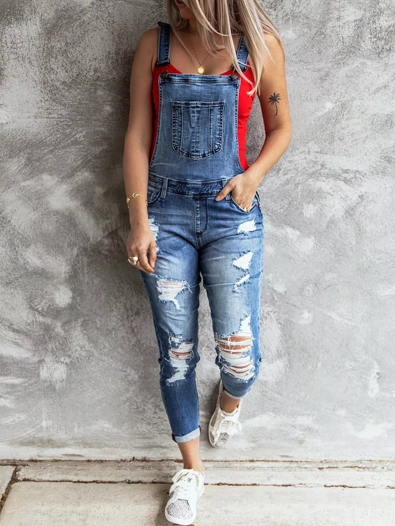 Person wearing a denim overalls with red straps against a gray wall.