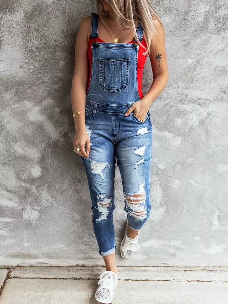 Person wearing a denim overalls with red straps against a gray wall.