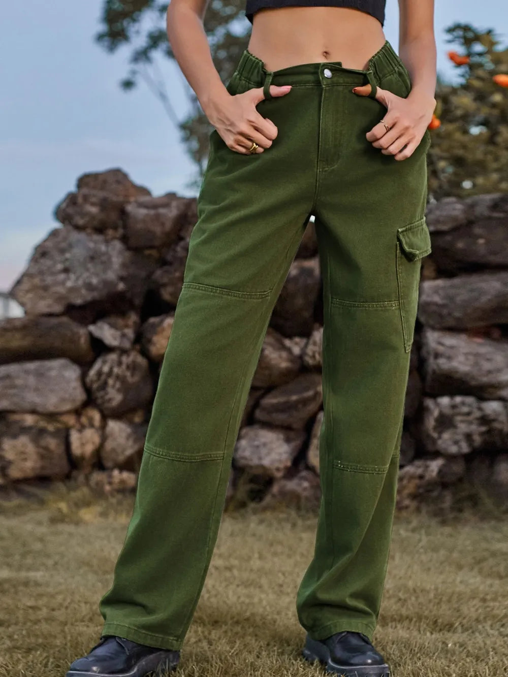 Person wearing green cargo pants standing in front of a stone wall.