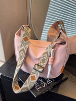 Pink handbag with patterned strap on a surface next to a book