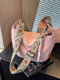 Pink handbag with patterned strap on a surface next to a book