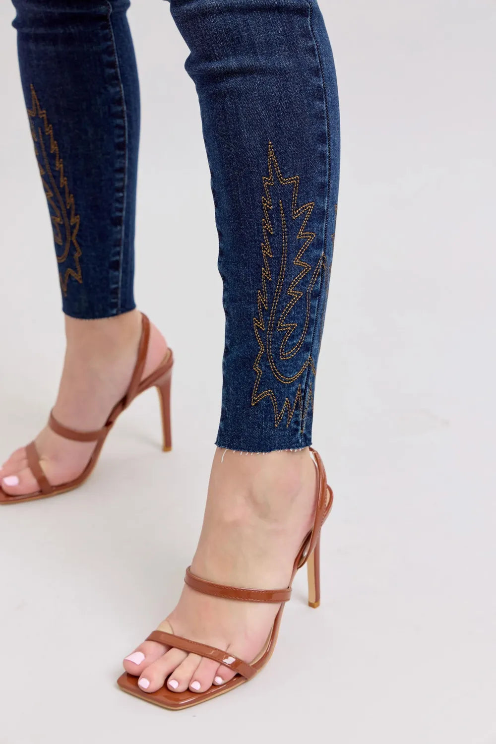 Close-up of blue jeans with embroidery and brown high-heeled sandals on a light gray background