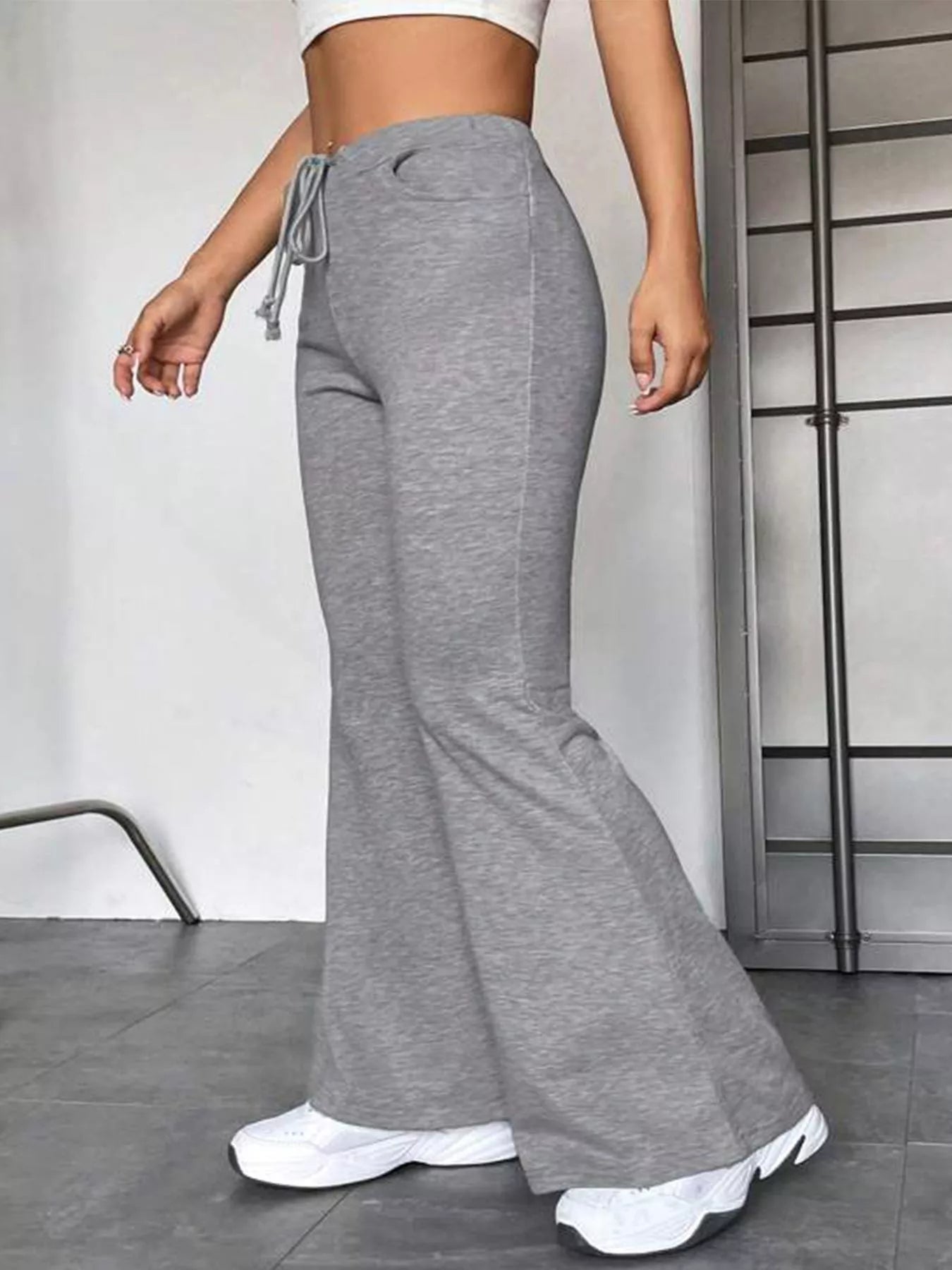 Person wearing gray flared pants and white sneakers in a minimal indoor setting