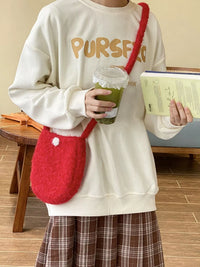 Person wearing a white sweatshirt with 'PURSEFUL' text, holding a red bag, green drink, and book.
