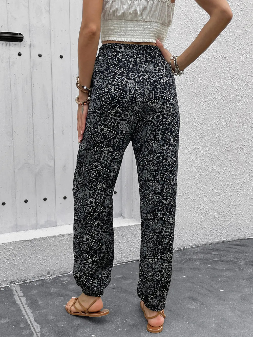 Person wearing black patterned pants standing against a gray wall.