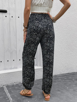 Person wearing black patterned pants standing against a gray wall.