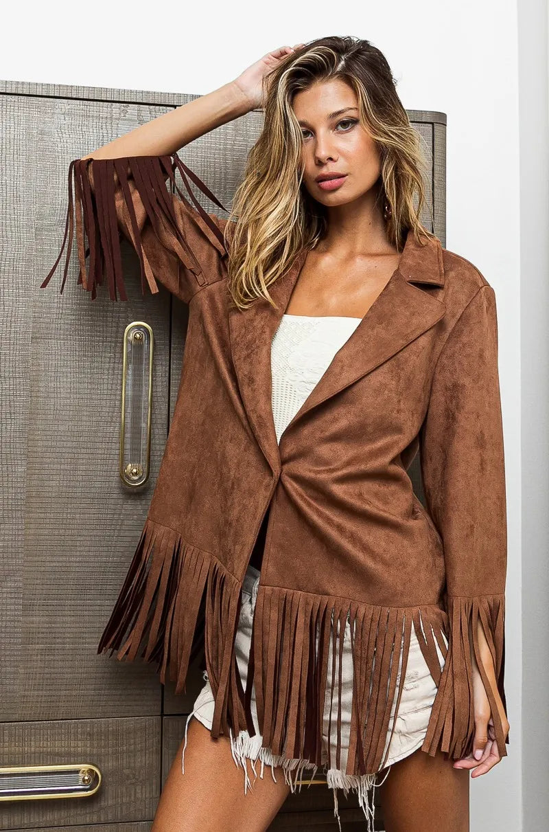 Woman wearing a brown suede jacket with fringe details against a neutral background