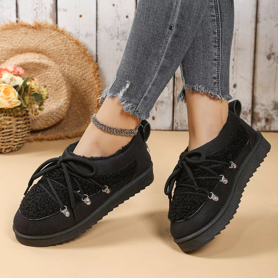 Black sneakers worn with ripped jeans on a wooden floor.
