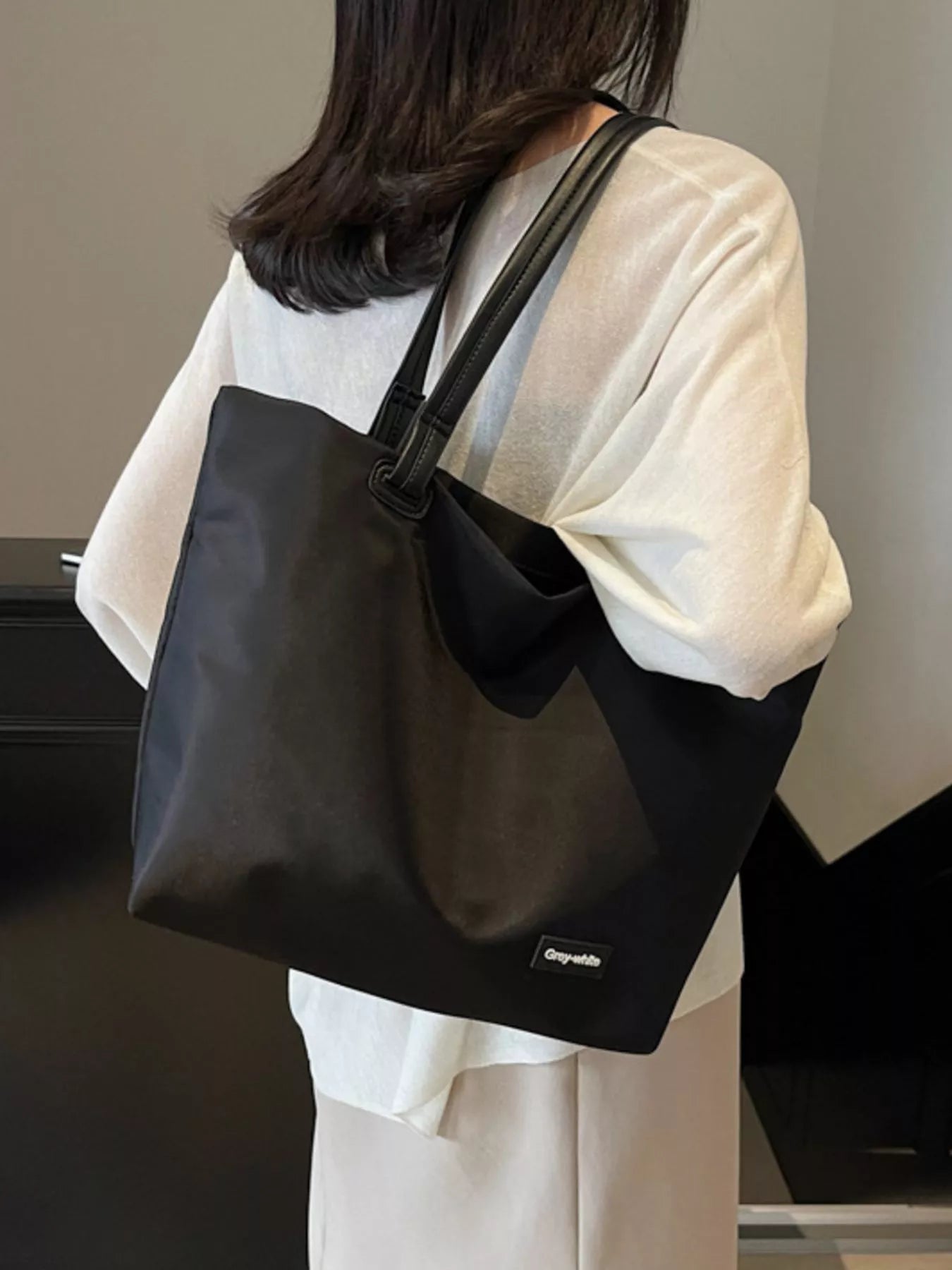 Person wearing a black tote bag with a visible brand logo.