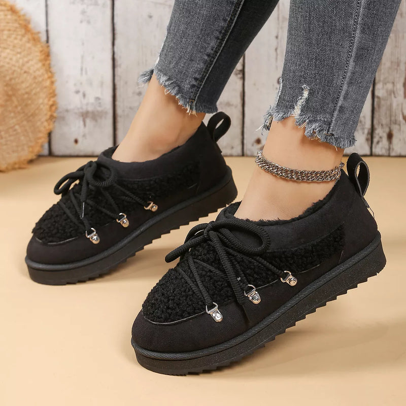 Black sneakers worn with ripped jeans on a wooden floor.