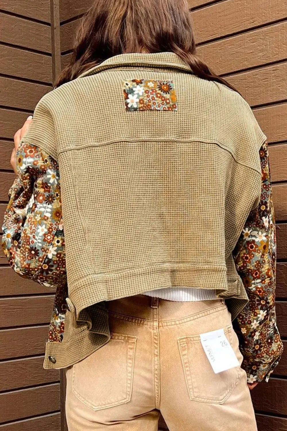 Person wearing a beige vest over a floral shirt with a wooden background