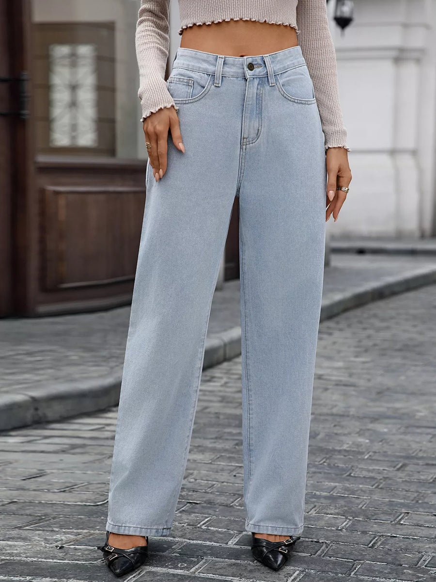 Person wearing light blue jeans and a beige sweater on a street.
