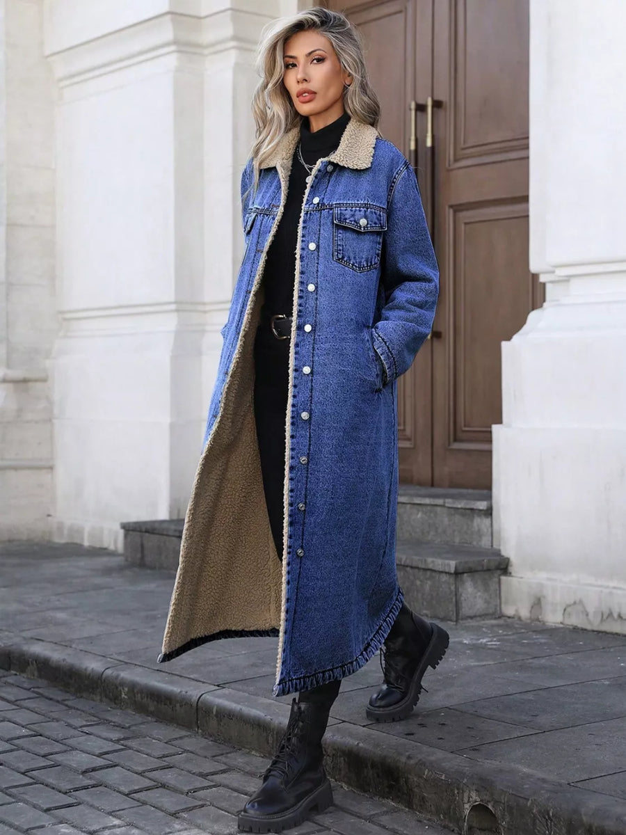 Woman wearing a long denim coat with beige interior standing on a street.