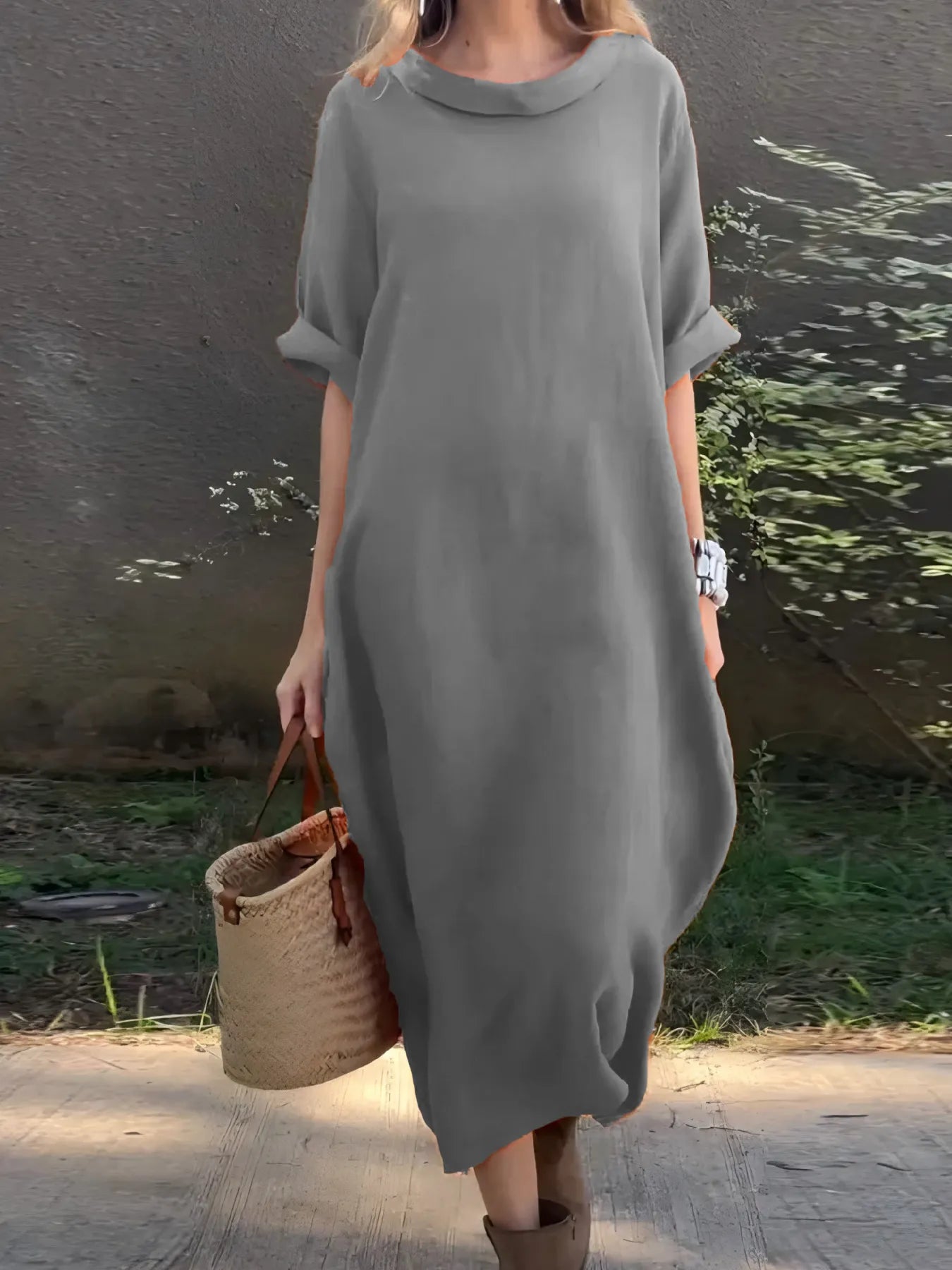 Person wearing a gray dress holding a woven bag outdoors.