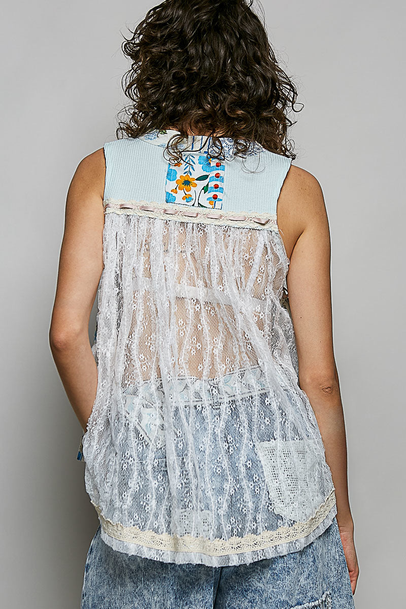 Person wearing a light blue sleeveless top with floral patterns on the back, standing against a plain background.