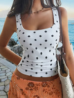 Woman wearing a white polka dot tank top and orange skirt by the sea.