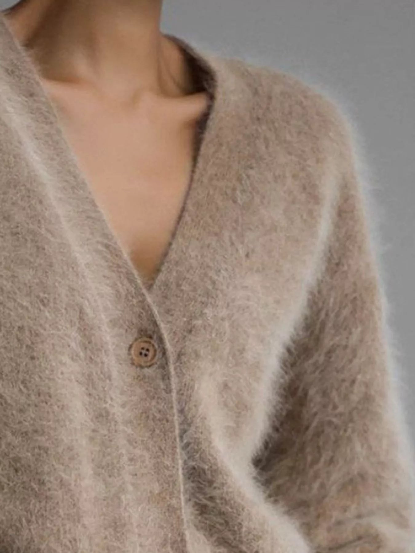 Close-up of a beige cardigan with a button on a neutral background
