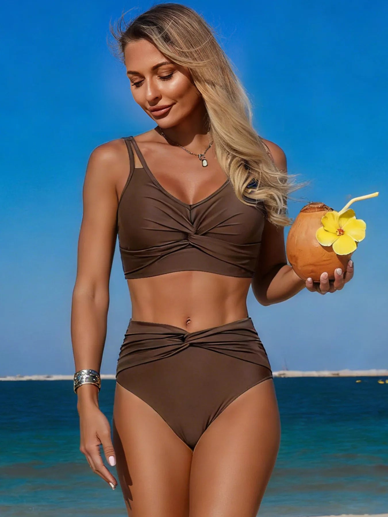 Woman in a brown bikini holding a coconut drink with a straw and flower on a beach.