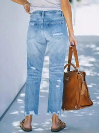 Person wearing light blue jeans holding a brown leather bag on a light background