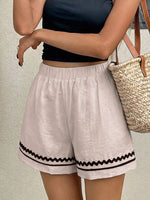 Person wearing light-colored shorts with black trim and a black top, holding a straw bag.