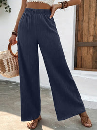Person wearing navy wide-leg pants with a white top and straw bag against a wooden door background.