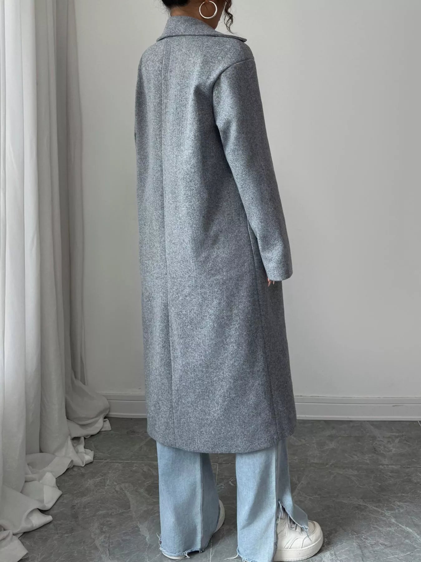 Person wearing a long gray coat in a minimal indoor setting