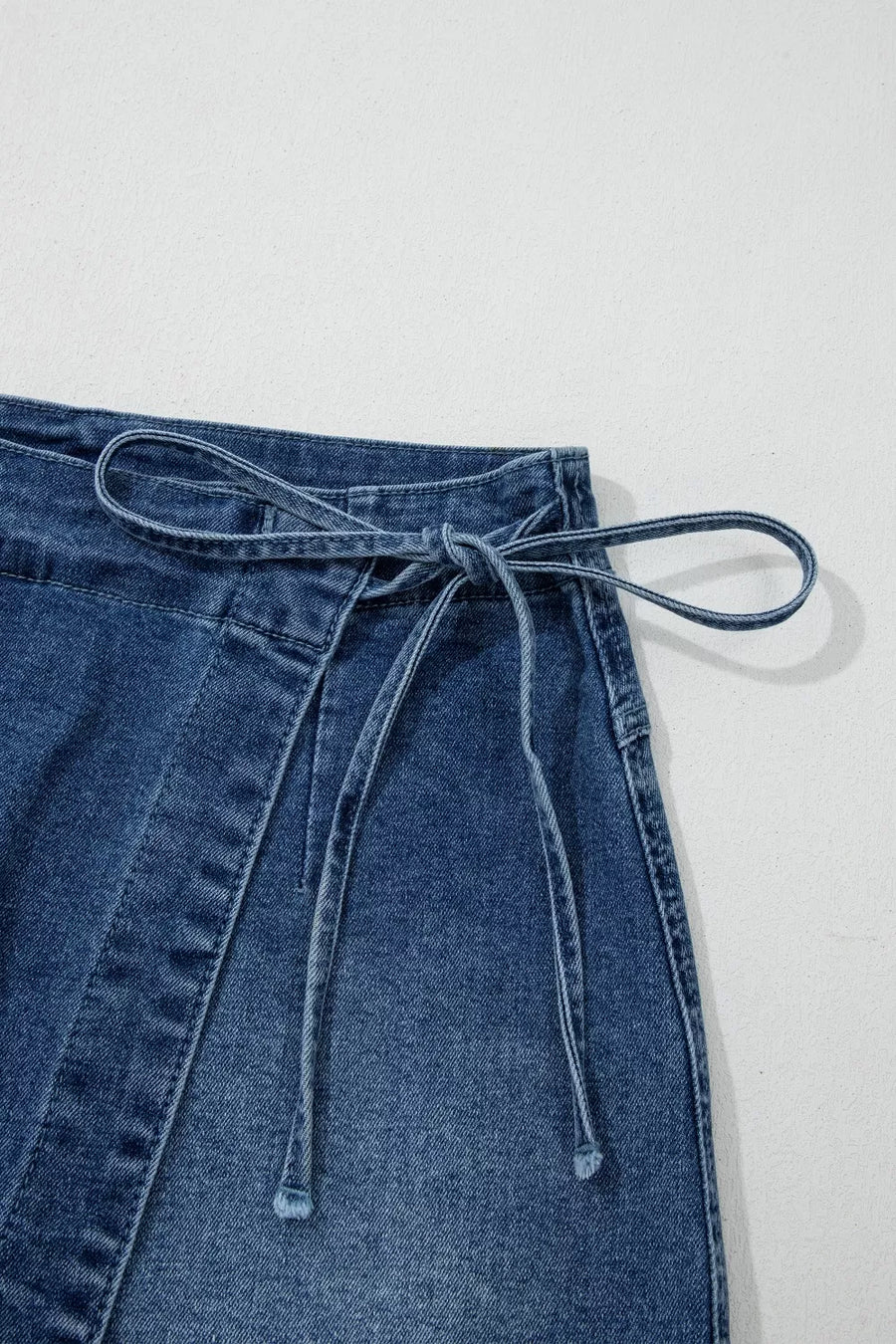 Blue denim skirt with tie waist on a light gray background