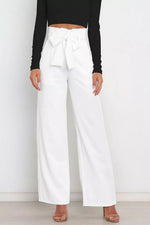 Person wearing white wide-leg pants with a black top on a plain background