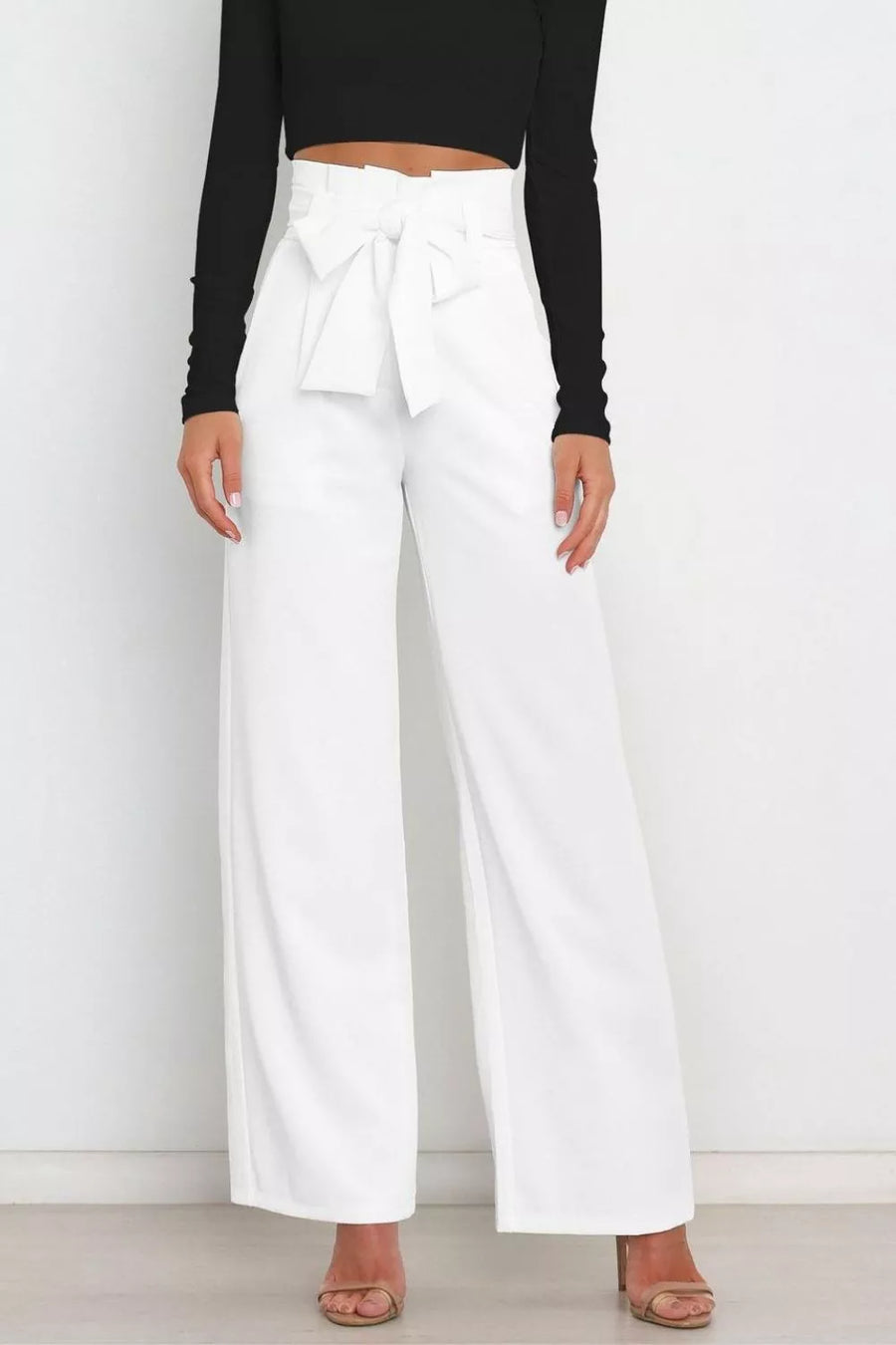 Person wearing white wide-leg pants with a black top on a plain background