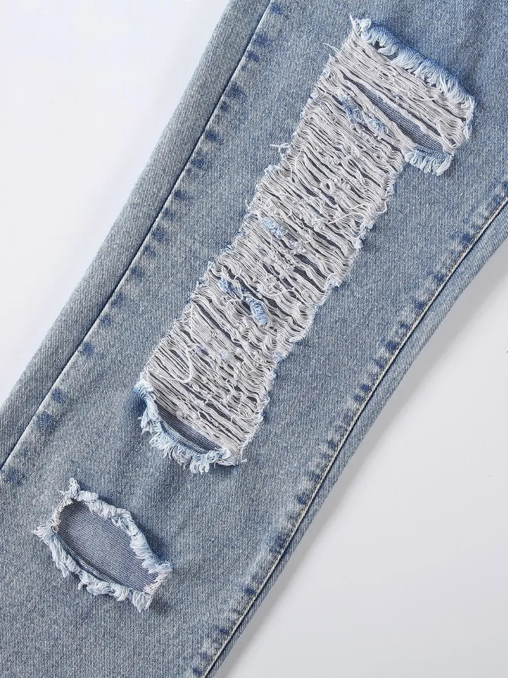 Distressed denim jeans with a large hole in the knee on a white background