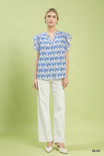 Woman wearing a blue floral blouse and white pants on a green background