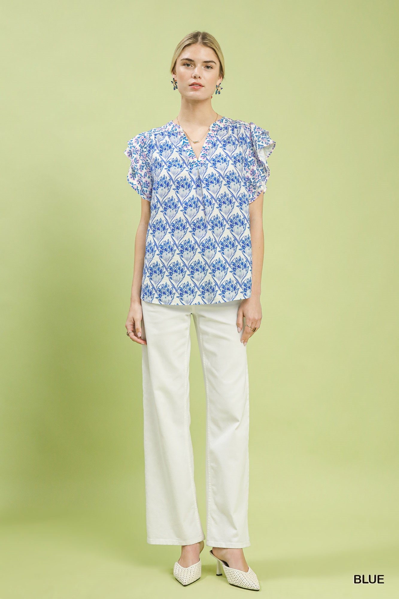 Woman wearing a blue floral blouse and white pants on a green background