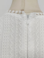 Close-up of a textured white garment with a zipper on a mannequin.