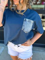 Person wearing a blue t-shirt with a denim pocket design, standing outdoors.