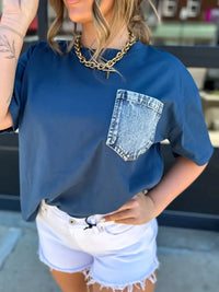 Person wearing a blue t-shirt with a denim pocket design, standing outdoors.