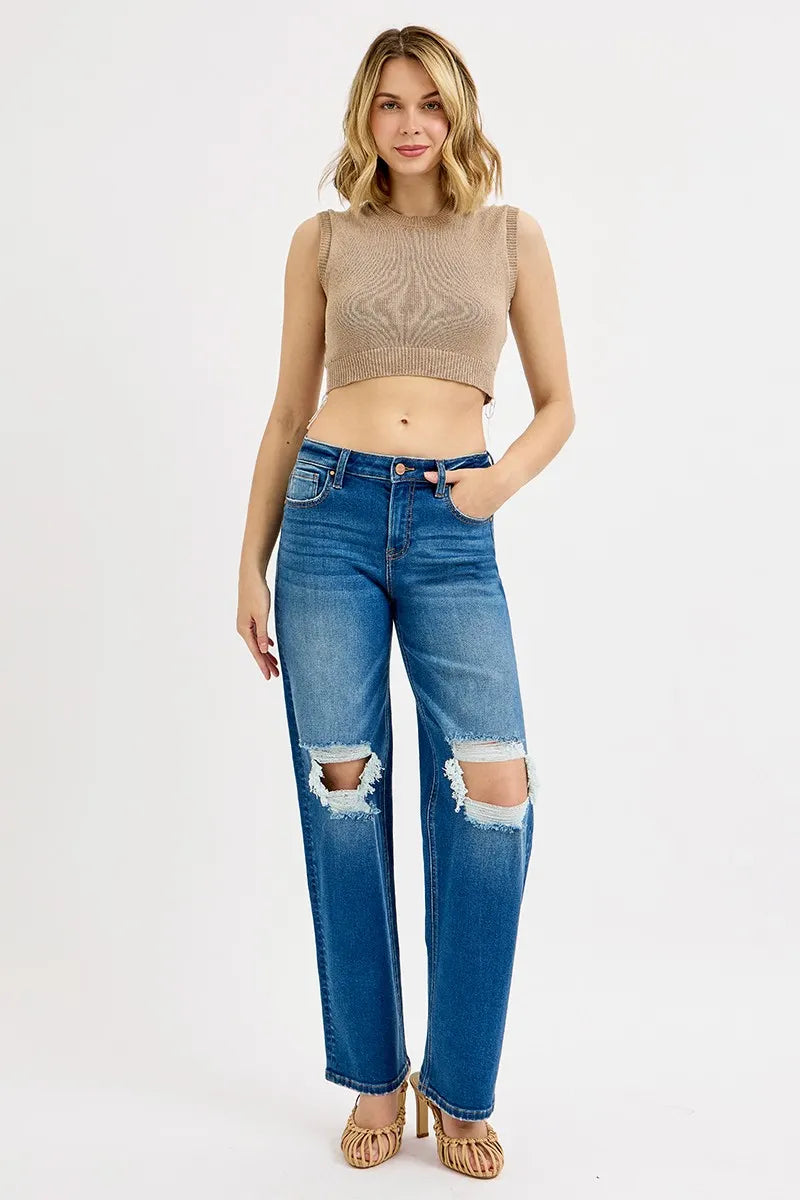 Woman wearing a beige sleeveless top and blue jeans with a white background