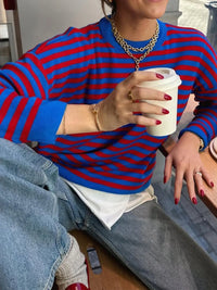 Person wearing a blue and red striped sweater holding a coffee cup.