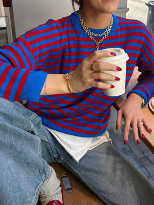 Person wearing a blue and red striped sweater holding a coffee cup.
