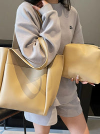 Person holding two beige bags, one large and one smaller, against a neutral background.