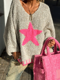 Person wearing a gray sweater with a pink star design, holding a pink textured bag.
