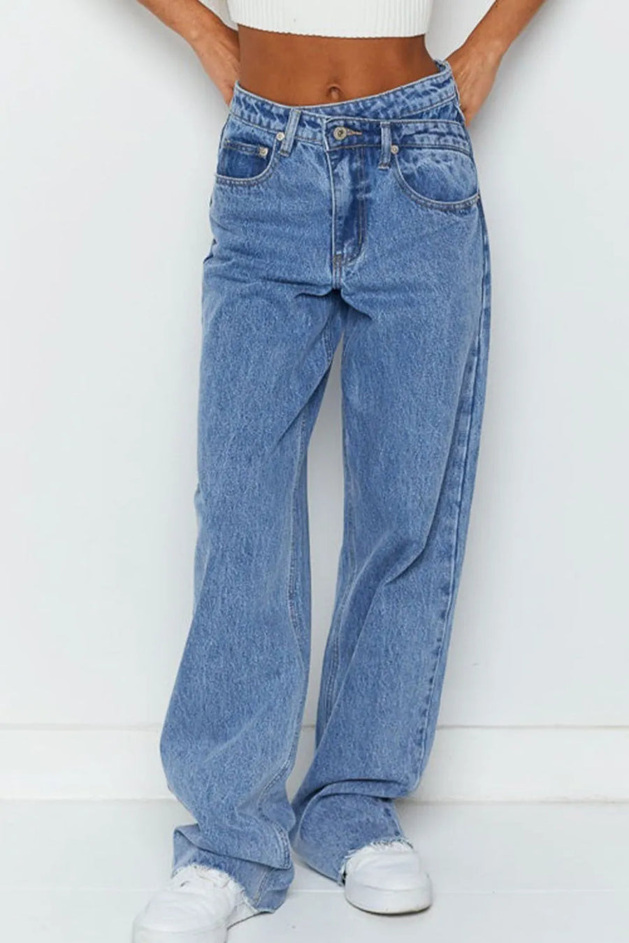 Person wearing blue jeans and white sneakers on a white background