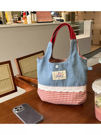 Blue and red checkered bag on a wooden table with a phone and a drink in the foreground.