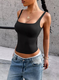 Person wearing a black tank top and blue jeans against a concrete wall.