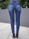 Person wearing blue jeans standing on a sidewalk with a blurred background