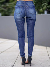 Person wearing blue jeans standing on a sidewalk with a blurred background