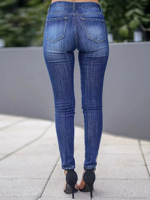 Person wearing blue jeans standing on a sidewalk with a blurred background