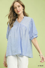 Woman wearing a light blue blouse with white pants on a green background